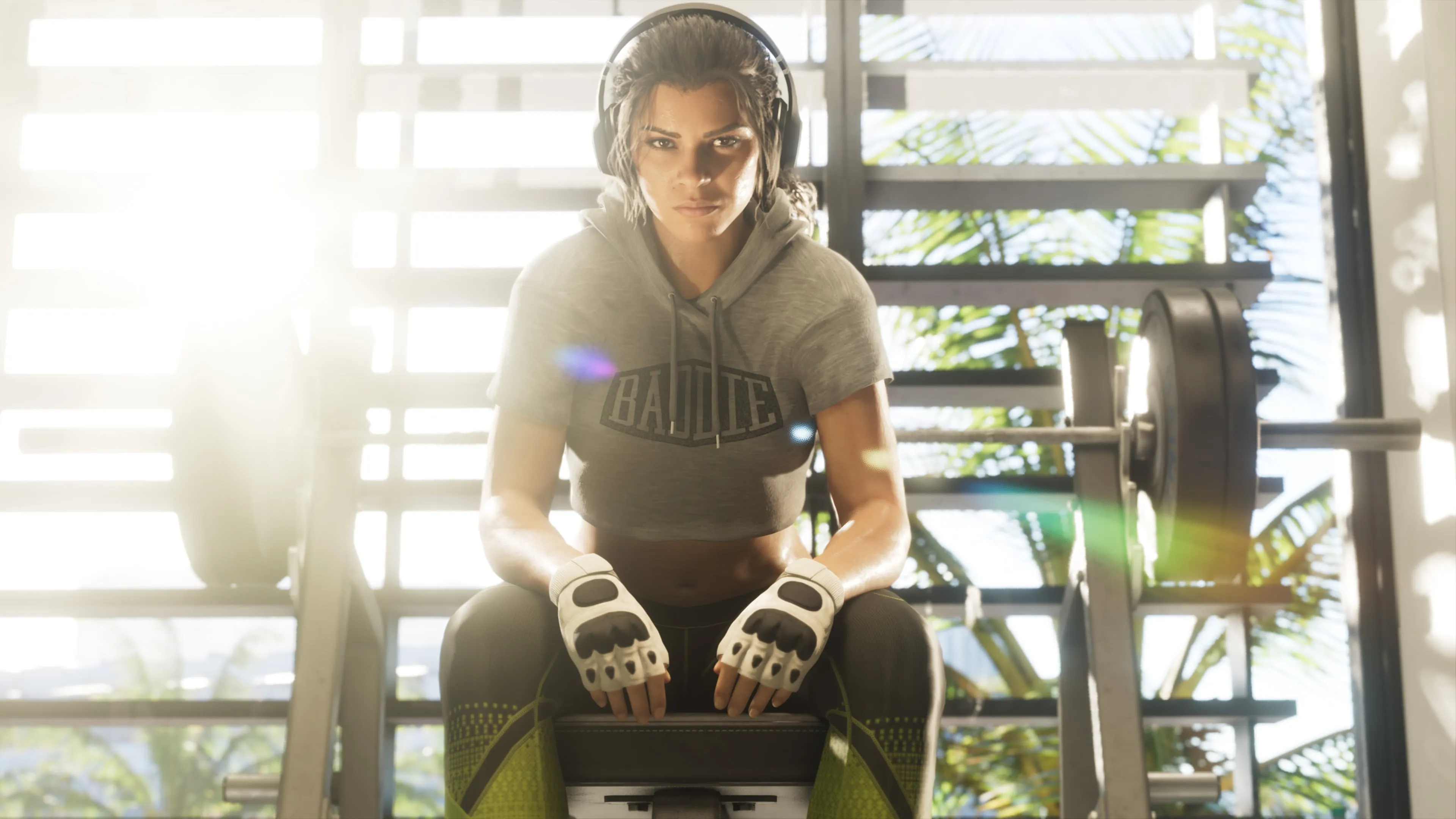 Lucia assise dans une salle de sport, portant un casque audio et des gants d’entraînement, devant des haltères.