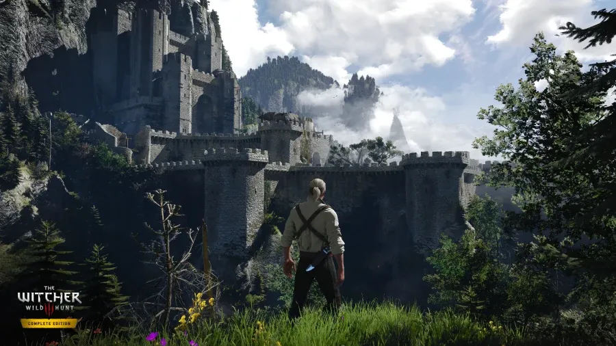 Avant : Geralt, vu de dos, contemple une forteresse de montagne entourée de forêts dans The Witcher 3 Complete Edition, avec des ombres très marquées au pied des remparts.
