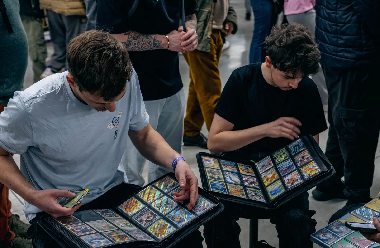 Deux visiteurs consultent des classeurs de cartes Pokémon au Gala TCG de la Paris Games Week.