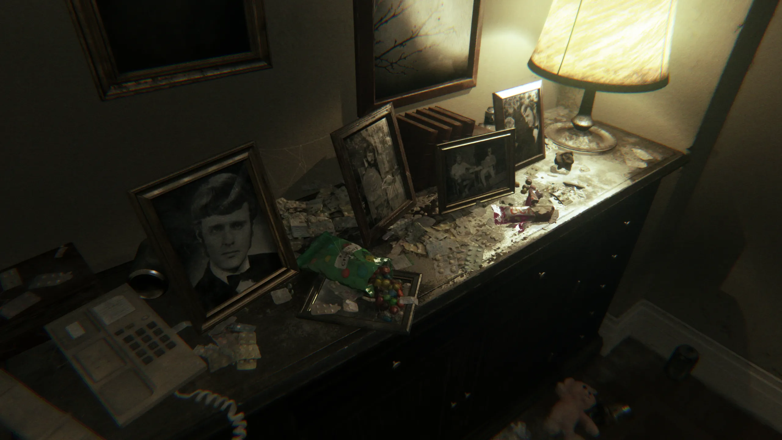 Un meuble de P.T. couvert de photographies, de débris et d’objets, éclairé par une lampe.