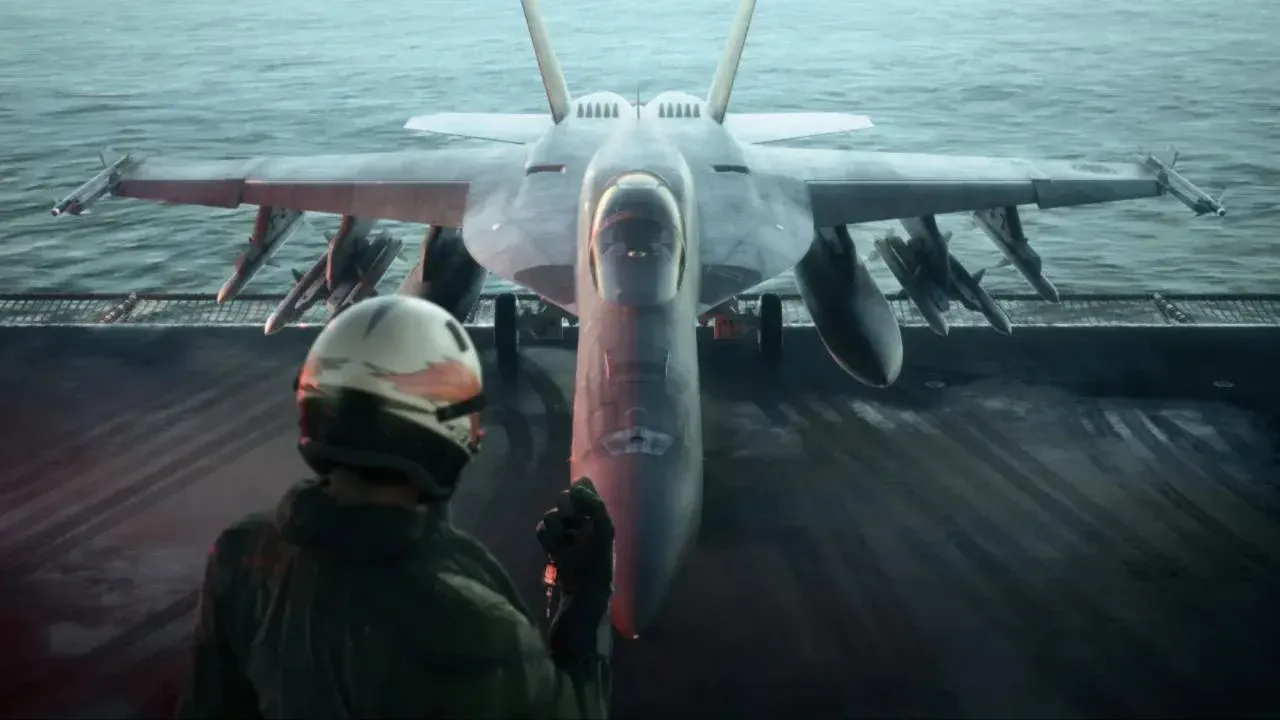 Un pilote casqué, vu de dos, sur le pont d’un porte-avions face à un chasseur armé de missiles, la mer en arrière-plan.