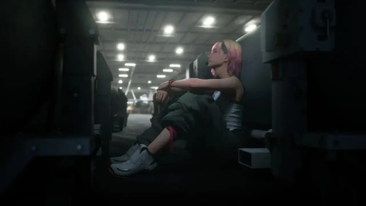 Tasha Severskaya, cheveux roses, assise seule contre une paroi dans un hangar éclairé au néon.